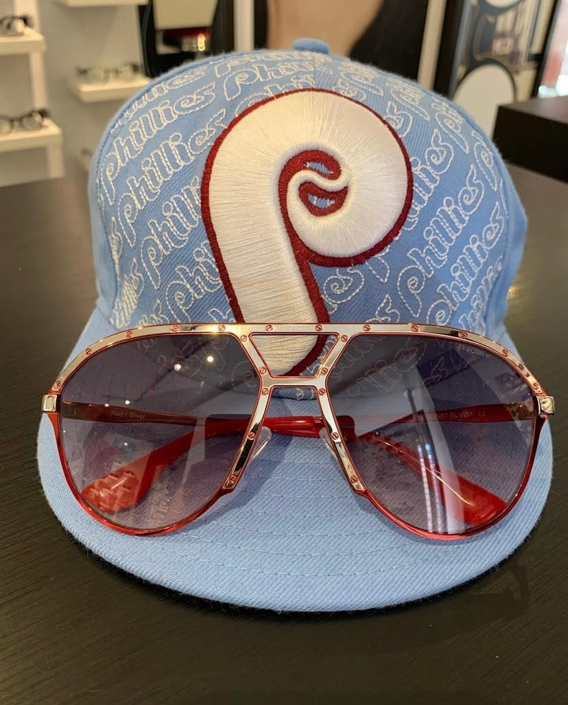 EYECON 87 Elvis 1 red and silver aviator frames resting on a Phillies cap